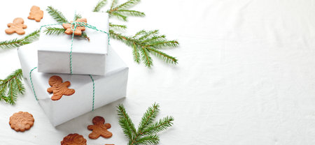 Christmas gifts wrapped in white paper and decorated with spruce sprigs and gingerbread cookiesの写真素材