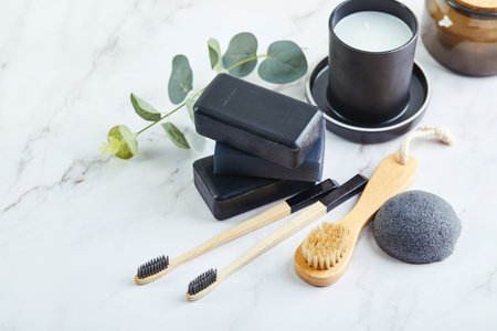 Pieces of black charcoal soap, Konjac sponge, beauty care products, candles, black charcoal toothbrushes and brushes for washing and massage on marble backgroundの写真素材