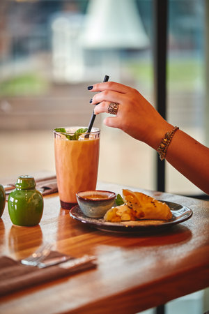 Woman's hand holds glass with milkshake or smoothie on wooden table in cafe against the background of window.の写真素材