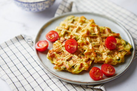 Savory waffles with bacon, cheddar cheese, spinach, sauce and cherry tomatoes on light backgroundの写真素材
