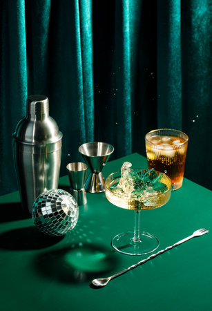 Splash in champagne glass, cocktail glass, shaker, cocktail spoon and jigger on dark green table in disco club atmosphereの写真素材