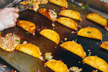Frying tacos tortillas with cheese, onion, herbs and meat on griddle in professional kitchen in...