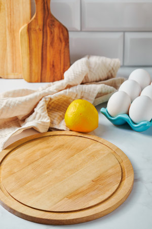 Round wooden cutting board, eggs and lemon on the kitchen table. Ingredients for preparing delicious mealの写真素材