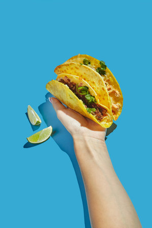 Two tacos on corn tortillas with beef, chicken and vegetable fillings in woman's hand on blue backgroundの写真素材