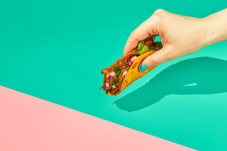 Female hand holding tacos on a color background. Mexican cuisine conceptの写真素材