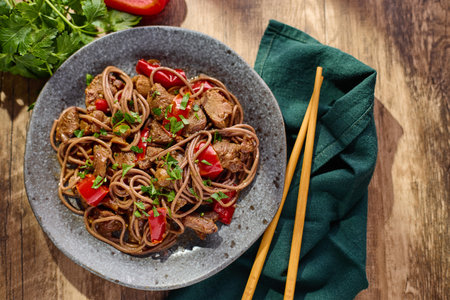 Wok with Soba noodles with turkey, mushrooms and sweet red bell pepper in plate on wooden table in...