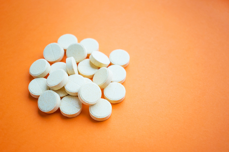 A pile of yellow ascorbic acid pills on an orange background. Synthetic Vitamin C. Prevention or treatment of the common cold. Dietary supplementの写真素材