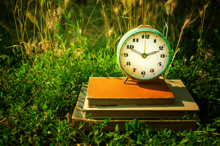 Vintage alarm clock on a stack of old books against a background of green grass. Copy space. Time concept, business planning.の写真素材