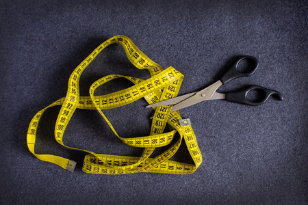 Metallic black scissors cutting a yellow tape measure on the background of gray cloth (greatcoat, woolen textile)の写真素材