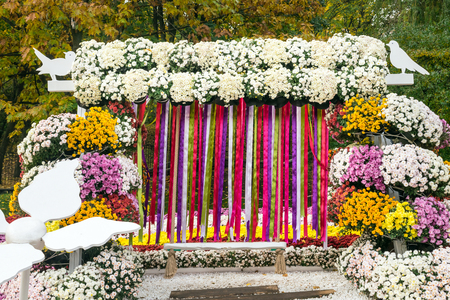 Beautiful flower chrysanthemum composition in the form of a swing with multi-colored ribbons. Floral decor for park and garden. Decorative composition of yellow white chrysanthemums. Landscape design ideaの写真素材