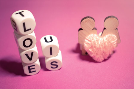 LOVE IS text word made with white plastic blocks, two wooden figures couple male and female and pink...