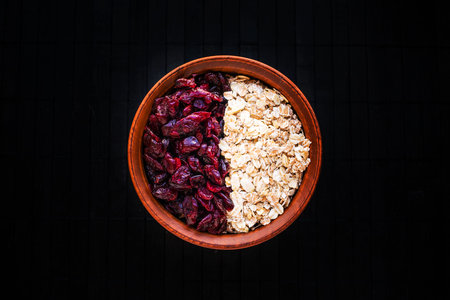 Raw oatmeal with dried cranberries in a round clay bowl on a dark wooden background. Healthy fitness...