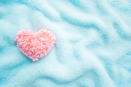 Fluffy pink thread heart on blue soft cozy fabric background. Handmade pretty heart. Love, romance, Valentines day DIY concept. Selective focusの写真素材