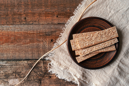 Whole-grained bread on a round brown clay plate on background of linen rough fabric and textured old wooden boards. Whole wheat low-calorie diabetic bread crispbread in rustic, wabi sabi style.の写真素材