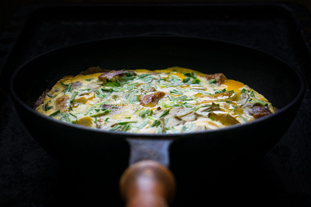 Scrambled eggs with herbs, bread, meat, onions and garlic in a frying pan on a dark background. Low...