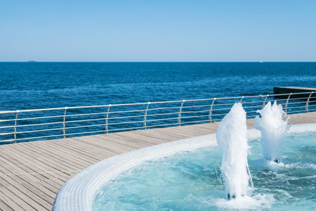 The gush of water of fountain. Splash and Foam of water. Blue vertical fountain with mosaic pool on the wooden terrace, by the sea. Rest on the beach, sea freshness in the summer heat. Siesta on the beachの写真素材