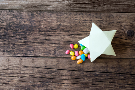 Sweet multicolored candy pills in paper gift box in the shape of yellow star. Sweet magical fairy-tale gift present. Candies, star gift box on wooden rustic background. Top view, flat lay, copy spaceの写真素材