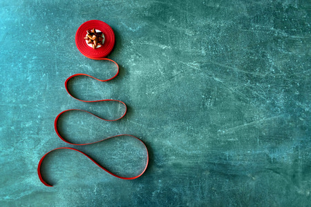 Decorative christmas tree made from red curly ribbon and red bow star on a dark blue textural background. Coil with red ribbon in the form of a xmas tree. DIY craft Christmas card, festive backgroundの写真素材