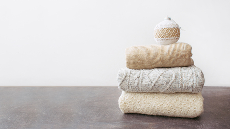 Pile of warm knitted sweaters with Christmas ornament and toy snowman on wooden table on light background. Winter cozy clothes background, mock up with copy space.の写真素材