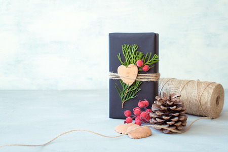 Christmas wrapping. Gift box, present with craft wrapping paper, twine, coniferous branches, red berries and scissors on grey concrete background. Wrapping christmas gift pack, decorationsの写真素材