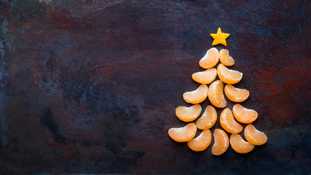 Tangerine christmas tree  on dark rust metal grunge background. Xmas festive greeting card with a tree of orange tangerine slices and star, copy space, flat layの写真素材
