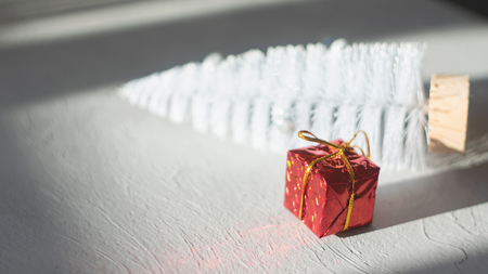 Modern minimal Christmas festive gift winter background. Close up red gift box, white Christmas tree, ornament ball on grey cement background. Xmas greeting card background, copy space, selective focusの写真素材