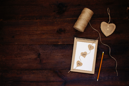 Declaration of love. Valentines day craft card ideas. Greeting card with text I LOVE YOU on craft recycled paper notebook, pencil, heart,  jute on wooden background. Love, romance, handmade conceptの写真素材