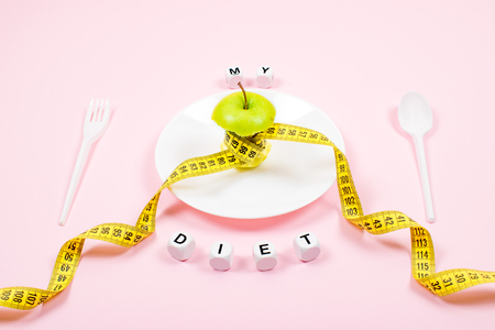 Apple core with measuring tape in place of the waist on a white plate with text MY DIET on pink background. Diet, weigh loss, starvation, fitness concept.の写真素材
