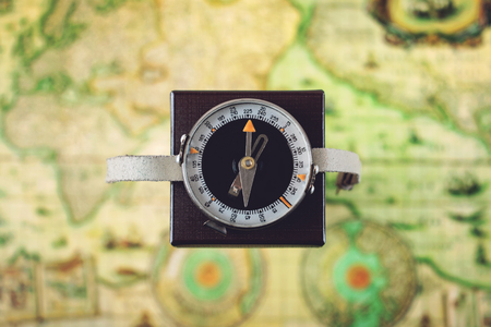 Compass heading north on square box against blurred green map background. Columbus day, travel, tourism concept.の写真素材