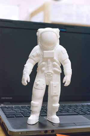 3D printed astronaut, cosmonaut, robot on the background of devices and laptop. Spaceman model...