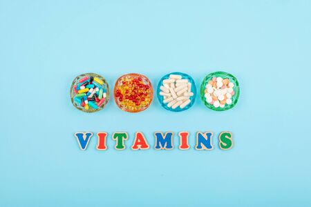 Different colorful pills and capsules in round plate and multicolored word VITAMINS on blue background. Nutrition supplement, drug, pharmaceutic concept.の写真素材