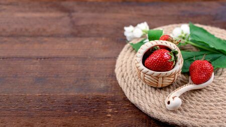 Summer background with straw round tray, strawberries in clay cup and white flowers with green leaves on wooden background. Summer berry vitamin background. Flat lay. Summer concept.の写真素材