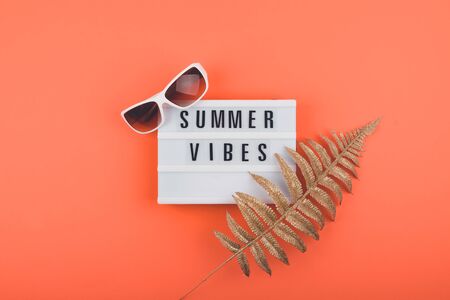 Summer vacations trip flat lay with Summer vibes text on light box, golden tropical leaves and Trendy white sunglasses. Colorful Hot Summer, vacations, travel concept.の写真素材