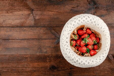 Fresh organic strawberries on round straw hat on brown rustic wooden background. Red berries on table flat lay.の写真素材
