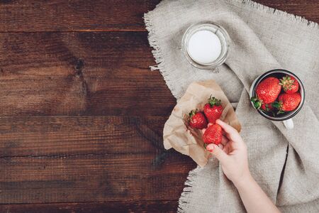 Child hand holding strawberry, sugar and cup of strawberries on linen cloth and rustic wooden background. Summer healthy eating concept with copy space. Top view, flat lay.の写真素材