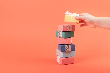 A stack of multi-colored gift boxes coral background. Many gift boxes with child hand.の写真素材