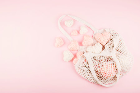 Reusable shopping net bag with white and pink knitted hearts on pastel background. Top view of eco...