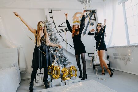 New Year Eve 2020 party. Celebrating of New Year. Three Happy Young girls with golden baloons 2020 celebrating new year. Young Woman in black cocktail evening dress Have Funの写真素材