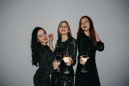 Party, holidays, celebration, nightlife people concept. New year celebration party in the club. Three beautiful women in black sparklers night fashion dress holding wineglass of alcoholの写真素材