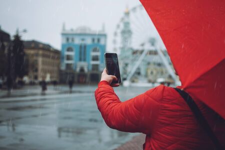 Girl with red umbrella taking photos in the rain. Woman traveler take pictures on rainy day.の写真素材