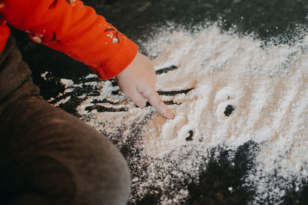 Flour Sensory Play for Toddlers. Easy flour sensory play activity for babies. Cute little girl sits on kitchen table and plays with flour.の写真素材