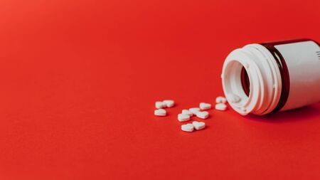 Blood-pressure, heart disease drugs. Small white heart shape pills with and bottle on red colorful background.の写真素材