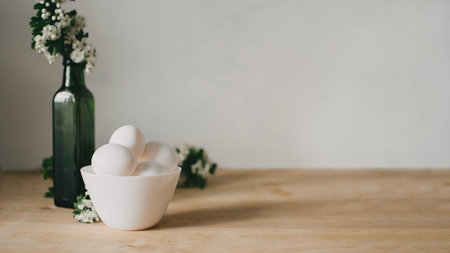 National egg day background with white eggs in bowl and flowers in green vase. National Egg Day on...