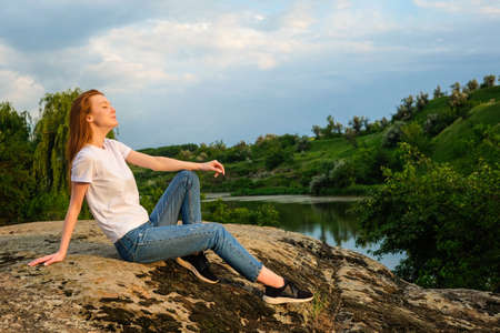 Relaxation, meditation mental health concept. National Relaxation Day. Red-haired woman meditates and relaxes in nature outdoor rocksの写真素材