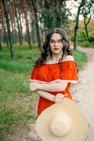 Local Domestic travel, green tourism . Summer time concept. Portrait of a beautiful woman in straw hat and red dress walking on rural roadの写真素材