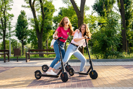 Three Young girl friends on vacation having fun driving electric scooter through the city park....