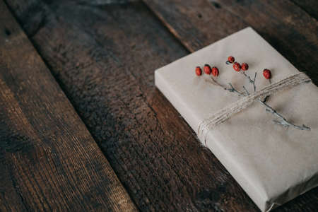 Eco-Friendly, Sustainable, zero waste christmas gift wrapped in kraft paper with twine and berry decor. Christmas wrapped gift box with natural decor on wooden backgroundの写真素材