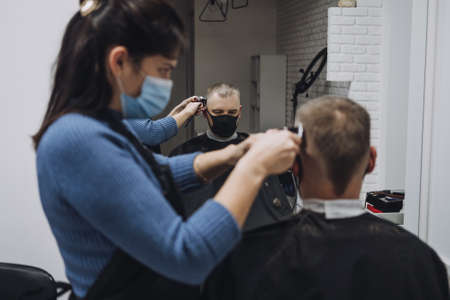 Barber shops, hair salons shutting down, second lockdown. Hairdresser in face mask peeling and combing male client in hair salon. Hairdresser and man client are wearing protective face masks.の写真素材