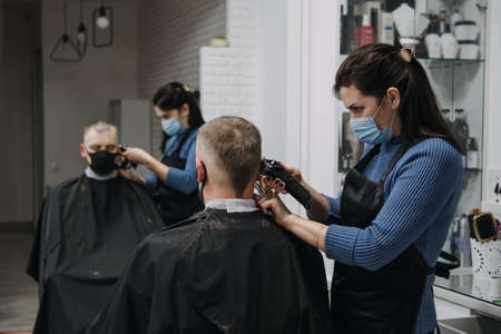 Barber shops, hair salons shutting down, second lockdown. Hairdresser in face mask peeling and combing male client in hair salon. Hairdresser and man client are wearing protective face masks.の写真素材