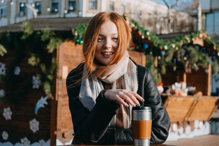 Young redhead woman enjoying the sun and drinking take away coffee wandering on winter city streets...